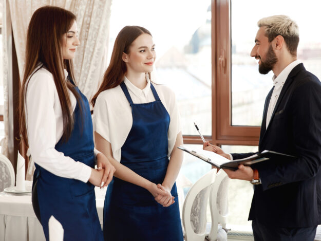 Handsome restaurant manager is talking to waitresses about work process